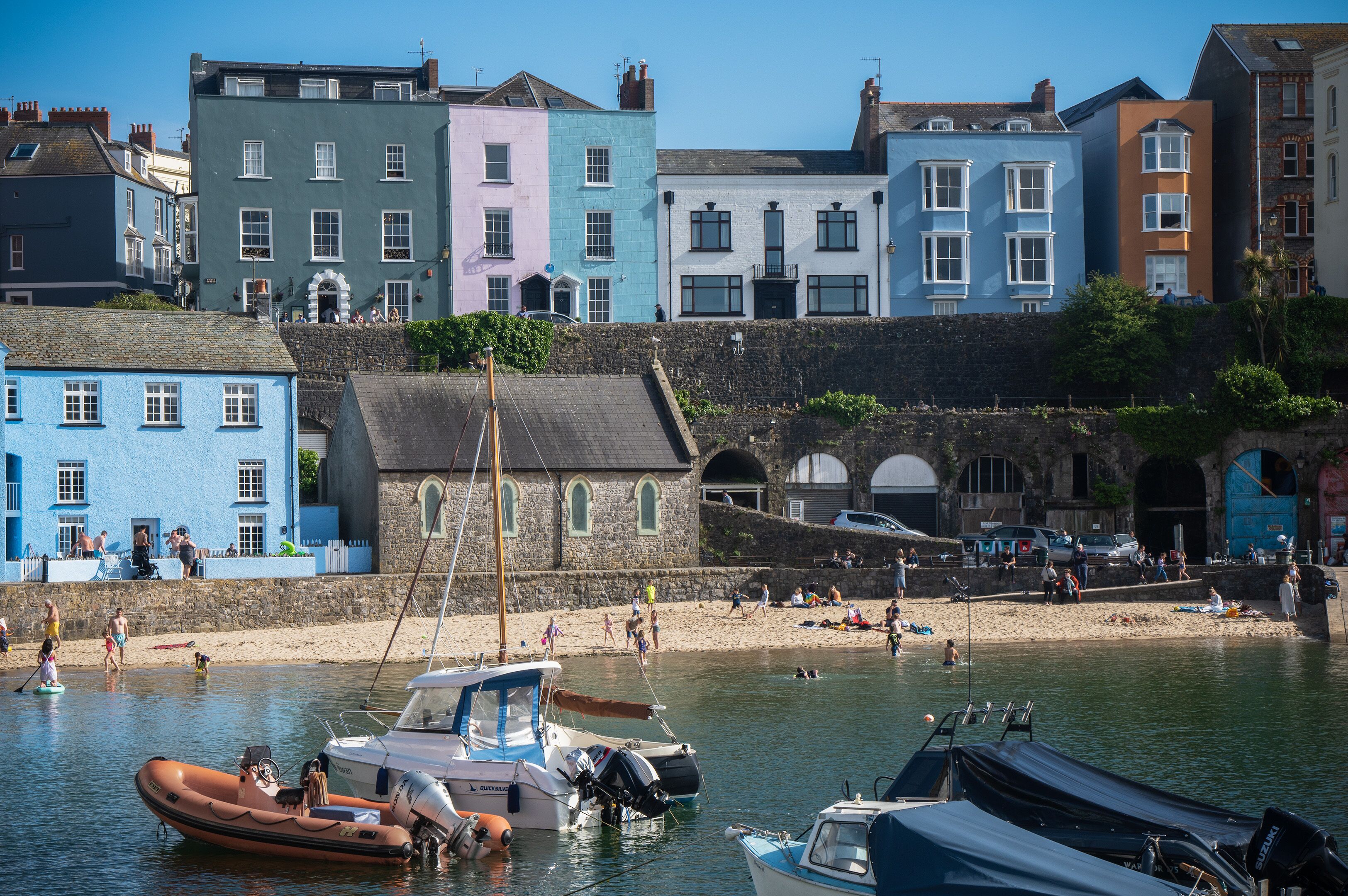 A coastal town with colorful buildings, a sandy beach, and boats docked at the harbor.