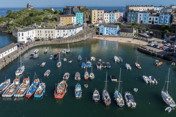 A harbor with numerous boats docked, surrounded by colorful buildings and a prominent hill with a structure on top. - Gwynne House - 6 Bedroom - Tenby Harbour (Tenby)