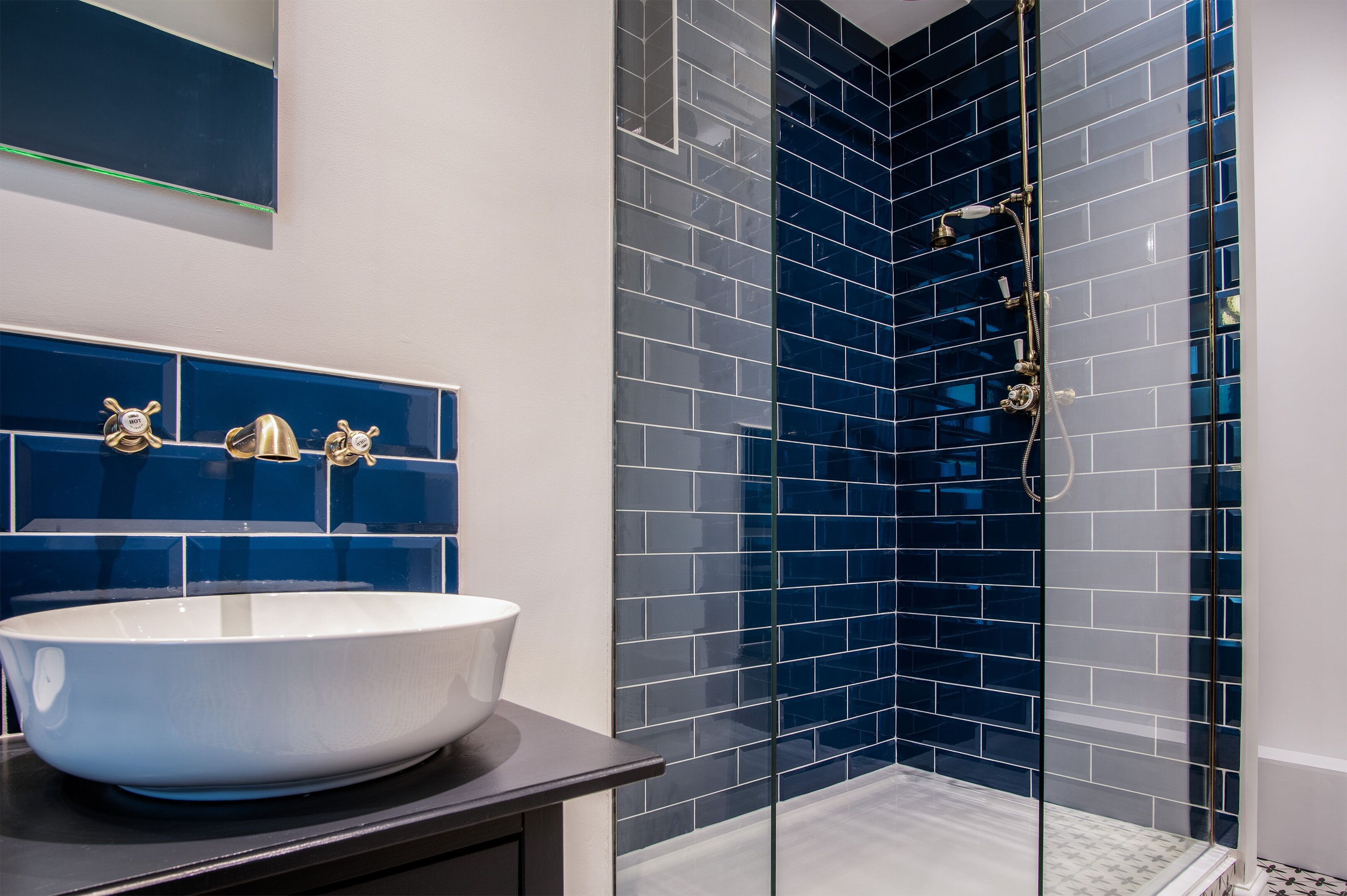 A modern bathroom with a large white vessel sink, blue-tiled shower enclosure, and a glass shower door.