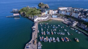 An aerial view of a coastal town with a marina filled with boats, historic buildings, and a prominent hill with a fort. - Gwynne House - 6 Bedroom - Tenby Harbour (Tenby)