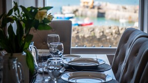 A dining table set with plates, glasses, and cutlery, overlooking a coastal view with boats and buildings. - Gwynne House - 6 Bedroom - Tenby Harbour (Tenby)