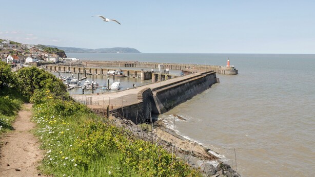 A coastal town with a sea wall, boats, and a lighthouse. - The Retreat (Watchet)