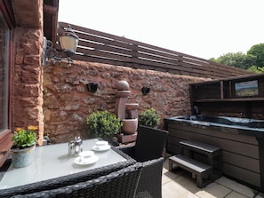 An outdoor patio with a stone wall, a hot tub, wicker furniture, and a table set with cups and saucers. - The Retreat (Watchet)