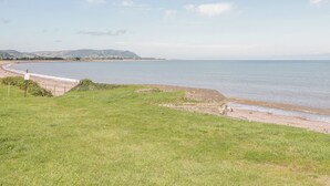 A coastal landscape with a grassy area leading to a sandy beach and a calm sea. - The Retreat (Watchet)