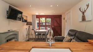 A modern kitchen with a wooden countertop, a sink, and a dining area with a table and chairs. - The Retreat (Watchet)