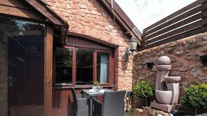 A stone building with a patio area featuring wicker furniture, a hot tub, and a stone sculpture. - The Retreat (Watchet)