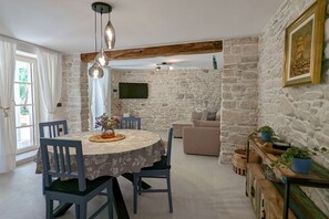 Un coin repas avec une table ronde, des chaises et un lustre. Un mur en pierre et un téléviseur fixé à ce mur complètent l’ensemble.