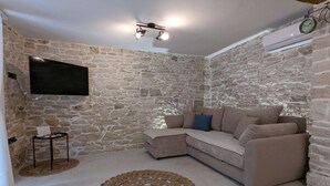 Una sala de estar con pared de piedra, un televisor de pantalla plana, un sofá, una mesita y un tapete decorativo.