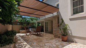 Un patio de piedra con pérgola, mobiliario exterior y plantas en macetas.