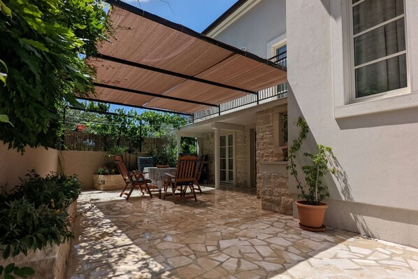 Une terrasse en pierre avec une pergola, des sièges d’extérieur et des plantes en pot.