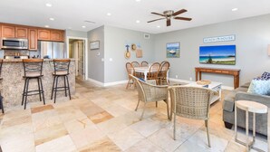 A spacious kitchen with granite countertops, a dining area with wicker chairs, and a living room with a gray sofa and a beach-themed wall. - 4 Bedroom Home Steps from the Sand w/ Balcony&BBQ (Newport Beach)