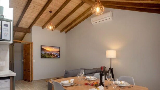 A dining area with a wooden table set for four, a grey sofa, and a painting of a sunset on the wall. - Sintra-Riviera by Interhome (Sintra)