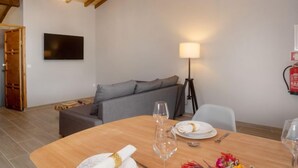 A dining area with a wooden table, a sofa, a TV mounted on the wall, and a lamp. - Sintra-Riviera by Interhome (Sintra)