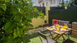 An outdoor patio with a table set for two, surrounded by greenery and a yellow wall. - Sintra-Riviera by Interhome (Sintra)