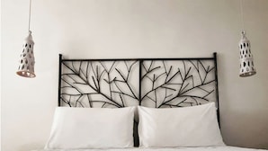 Ein Bett mit weißer, strukturierter Bettdecke, zwei weißen Kissen und einem schwarzen Metall-Kopfstück mit Blattmuster.