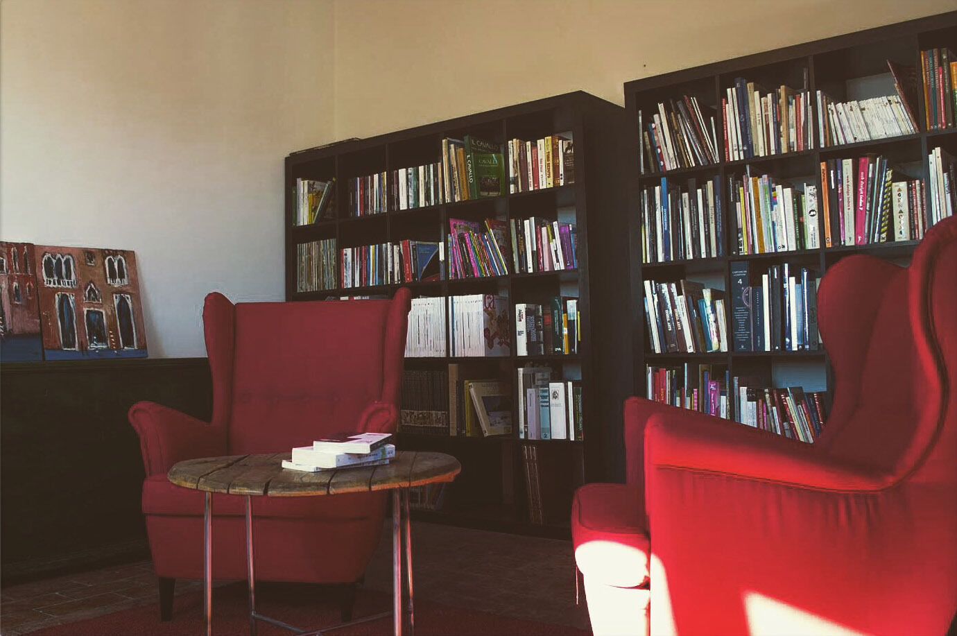 A library with two red armchairs and a small table, surrounded by tall bookshelves filled with books.