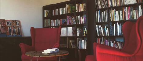 A library with two red armchairs and a small table, surrounded by tall bookshelves filled with books.
