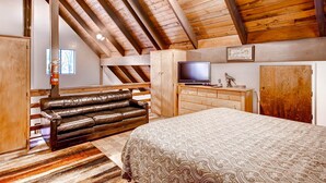 Un acogedor dormitorio estilo loft con una cama grande, un sofá de cuero, un televisor y un armario de madera.