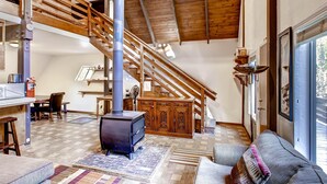 Un amplio espacio habitable con techo alto, escalera de madera, chimenea y un ventanal grande.