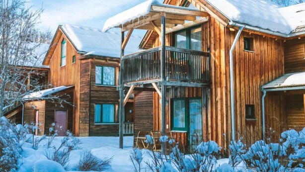 Una cabaña de madera con balcón, rodeada de nieve y árboles.