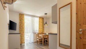 Una habitación compacta con puerta de madera, una mesa de comedor con sillas, un televisor montado en la pared y una ventana con cortinas.
