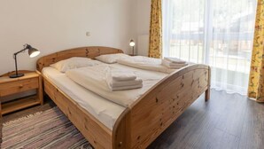 Una cama de madera con sábanas blancas, una lámpara de noche y una ventana con cortinas de encaje.