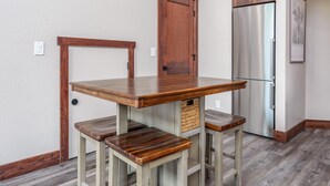 Una cocina con una mesa de madera y taburetes de bar, un refrigerador y una puerta con picaporte.