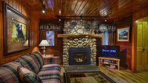 A cozy cabin interior with a plaid sofa, a stone fireplace, a television, and framed artwork. - Bear Foot Pines (CA 95389)