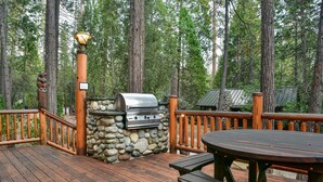A wooden deck with a stone barbecue grill, wooden railings, and a picnic table. - Bear Foot Pines (CA 95389)