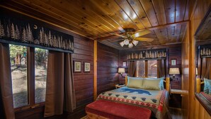 A wooden cabin room with a bed, a ceiling fan, and a window with curtains. - Bear Foot Pines (CA 95389)