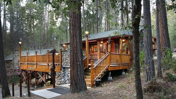 A wooden cabin with a stone foundation, wooden deck, and a staircase leading to the main entrance. - Bear Foot Pines (CA 95389)