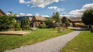 Ländliche Umgebung mit Holzhütten, einem Spielplatz und einem Kiesweg.