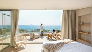 A bedroom with a large bed, a balcony with a view of the sea, and a sitting area with chairs and a table. - Luria Homes (Sithonia)
