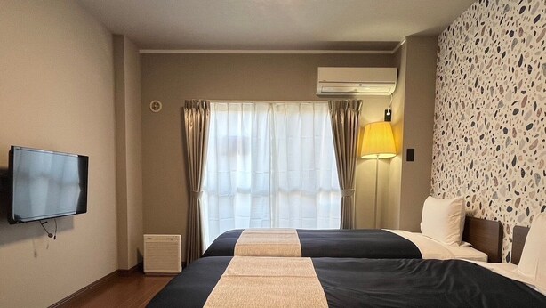 A hotel room with two beds, a television, an air conditioner, a lamp, and a window with curtains. - Stay Airport (Fukuoka)