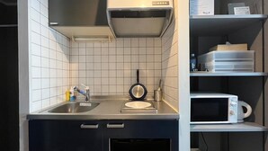 A compact kitchen with a sink, a frying pan, a microwave, and a built-in oven. - Stay Airport (Fukuoka)