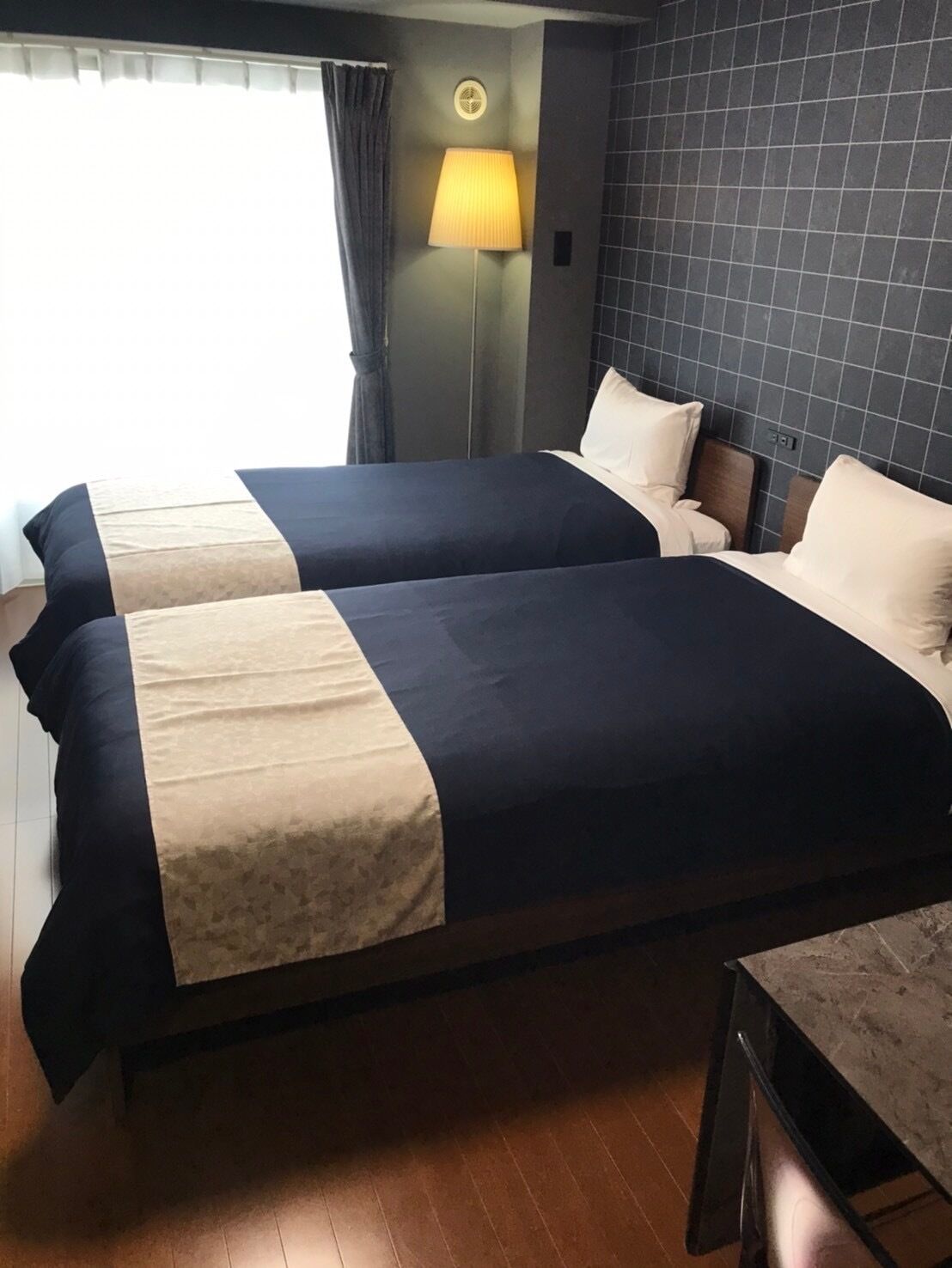 A hotel room with two beds, a nightstand, a lamp, and a view of the outdoors.