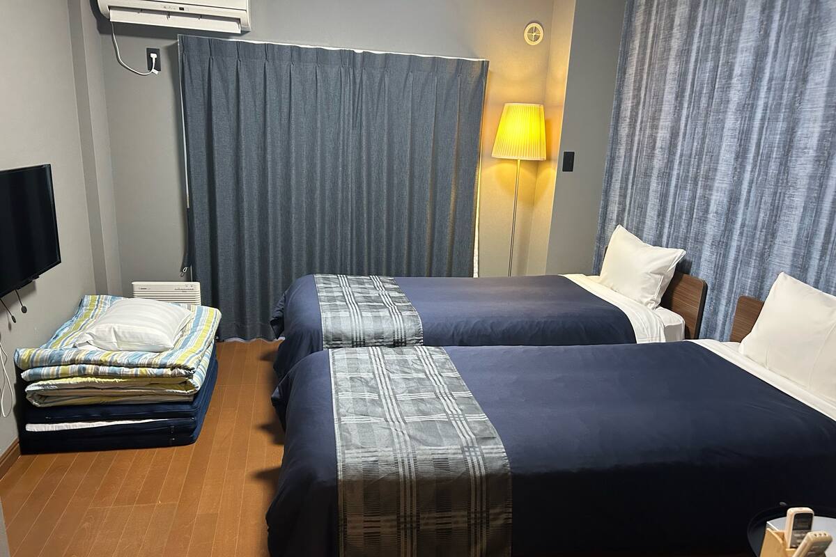 A hotel room with two beds, a flat-screen TV, an air conditioner, a lamp, and a bedside table with a phone.