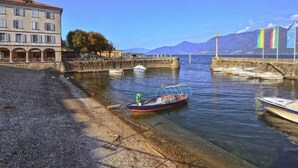 A waterfront with boats docked, a building with arches, and mountains in the background. - Angelina by Interhome (Luino)