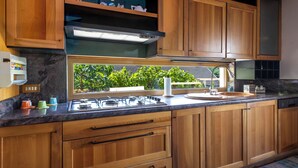 A kitchen with wooden cabinets, a gas stove, a sink, and a window with a view of greenery. - Angelina by Interhome (Luino)