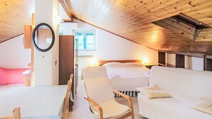 Ein gemütliches Zimmer mit Holzbalkendecke, einem Bett, einem Sofa, einem Schaukelstuhl und einem Tisch.