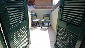 Ein schmaler Gang mit grünen Fensterläden, der zu einer kleinen Außenbereich-Sitzgelegenheit mit zwei Stühlen und einem Tisch führt.