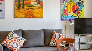 Ein Wohnzimmer mit grauem Sofa, farbenfrohen Kissen, einem Flachbildfernseher und zwei Bildern an der Wand.