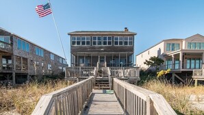 Une promenade en bois mène à un bâtiment doté de nombreuses fenêtres et surmonté d’un drapeau.