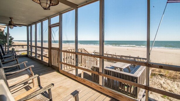 Une chambre située en bord de mer, dotée de grandes fenêtres, d’une terrasse en bois et offrant une vue sur l’océan.