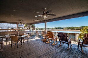 Una terraza de madera con mesa y sillas, un ventilador de techo y vistas a un río.