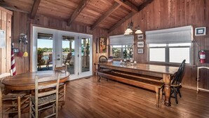 Un intérieur en bois avec une grande table à manger, des chaises et un banc. On y trouve des portes donnant sur l’extérieur, un extincteur et une fenêtre avec des stores.