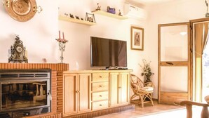 Een woonkamer met een open haard, televisie, houten kast en een fauteuil.
