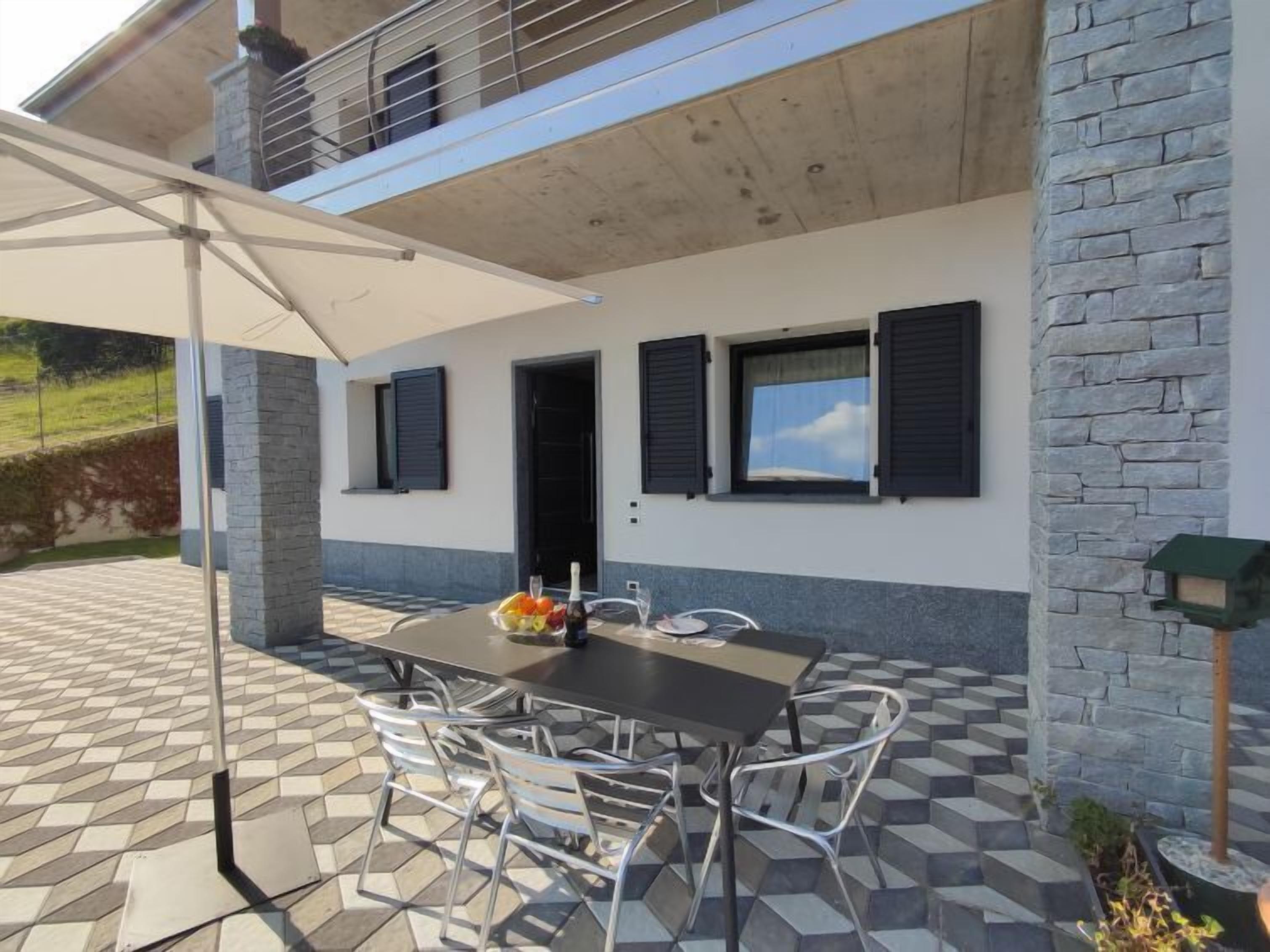 Eine Terrasse im Freien mit Tisch und Stühlen, einem weißen Sonnenschirm und einer Steinmauer.