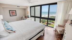 A bedroom with a large bed, a chair, a desk, and a view of the beach. - Paradise Found Beachfront Litchfield By the Sea (Pawleys Island)