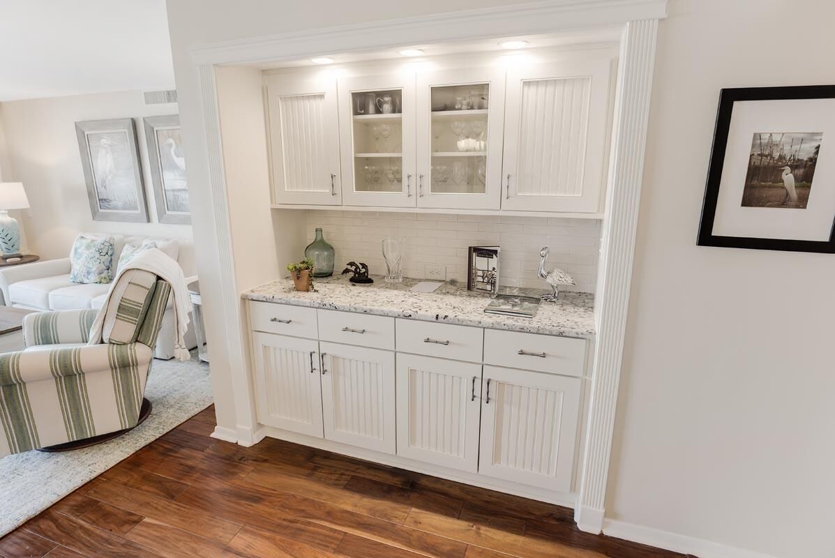 A kitchen with white cabinetry, a marble countertop, and a dining area with a striped chair.
